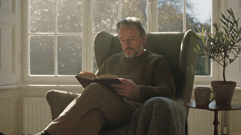 An older man reading comfortably beside a window